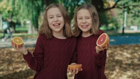 two caucasian sisters holding oranges and grapefruit on their eyes in autumn.