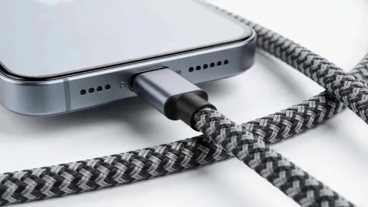Camera zooming on phone bottom edge, highlighting seated braided cable connector on white surface