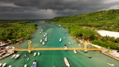 Gelbe-Brücke-über-Das-Klare-Wasser-Des-Meeres-Mit-Fischerbooten-Und-Segelbooten-An-Bewölkten-Tagen-In-Nusa-Lembongan,-Indonesien