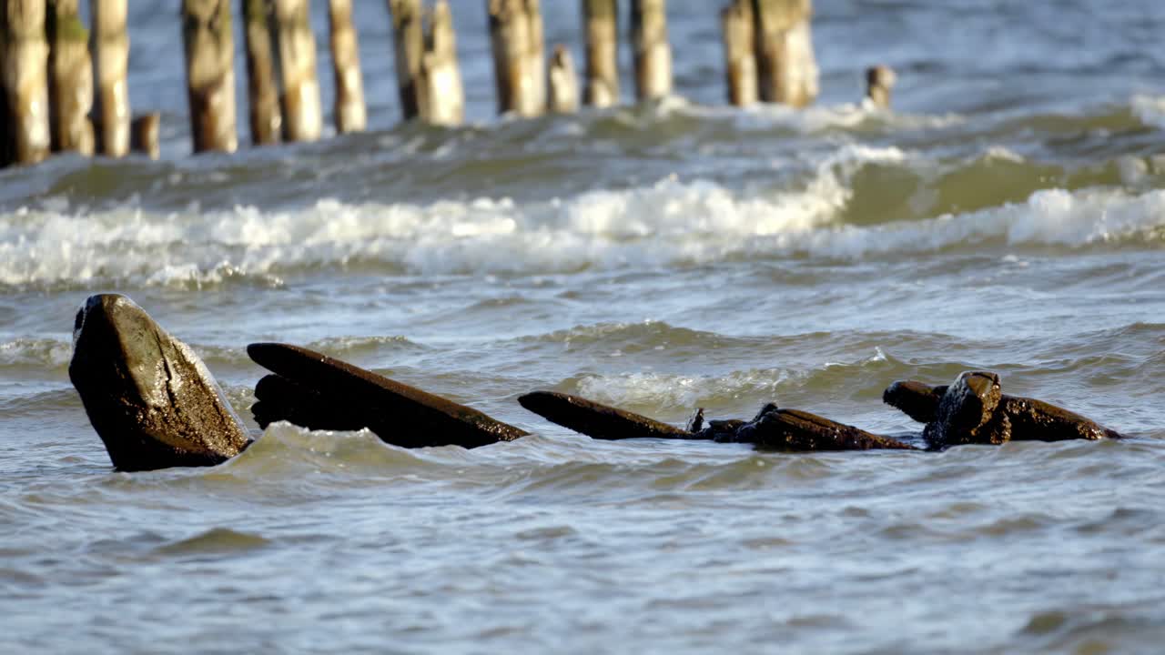 restos de un gran naufragio de madera en una playa de arena, con aguas tranquilas y azules en el fondo