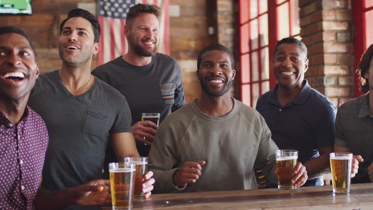 grupo de amigos masculinos celebrando mientras ven el juego en la pantalla en un bar deportivo