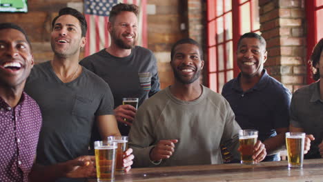 group of male friends celebrating whilst watching game on screen in sports bar