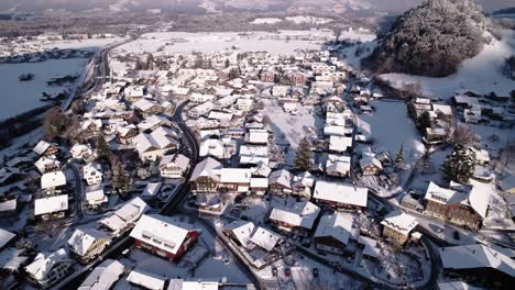 Aerial-view-of-snow-covered-mountains,-villages-and-forests-in-Switzerland-on-a-sunny-winter-day