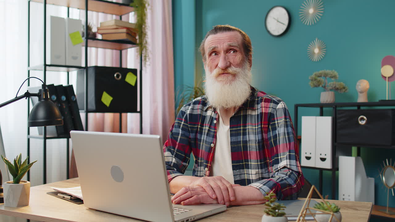 Thoughtful concerned senior man working on laptop computer looking away thinking solving problem