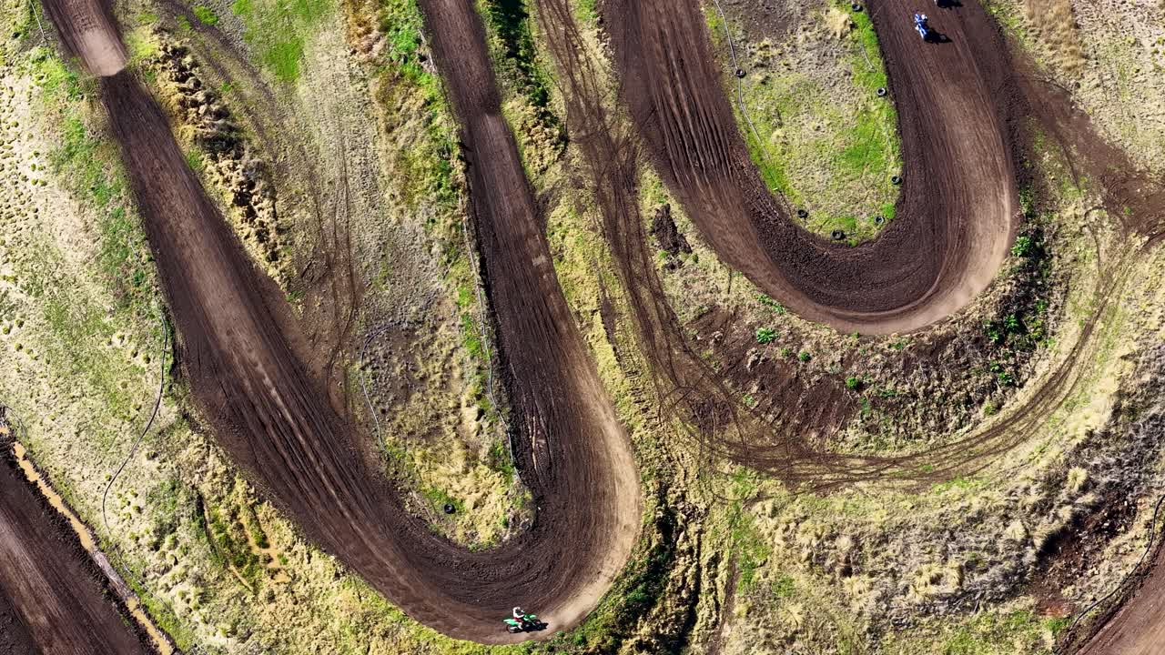 Motorcykler suser rundt i et sving på en jordbane, fanget i stærkt dagslys fra en drone ovenover