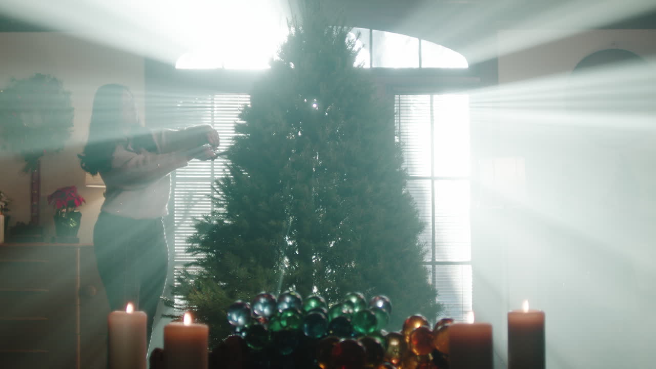 A woman decorates a Christmas tree with festive lights and candles