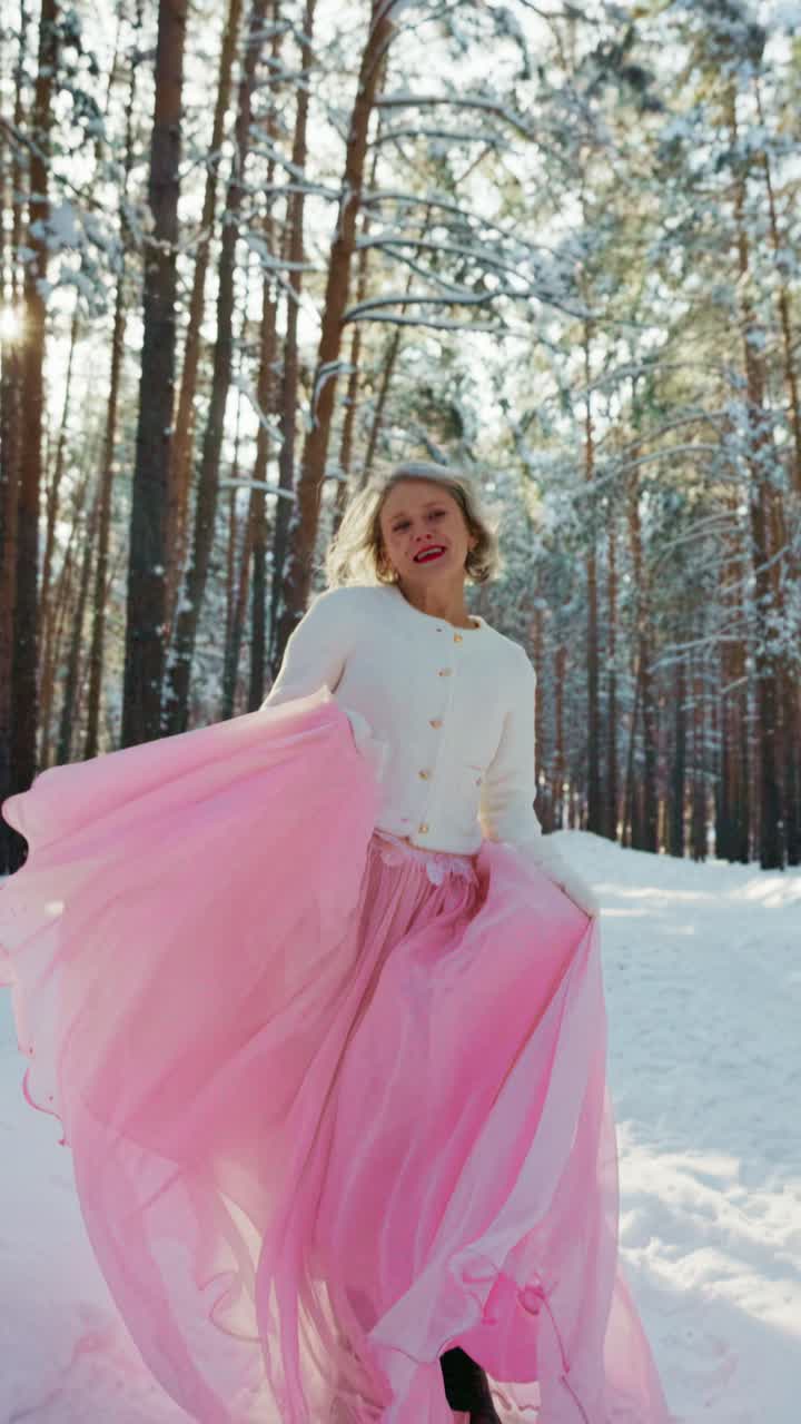 Donna gioiosa in gonna rosa che si diverte in una foresta invernale innevata