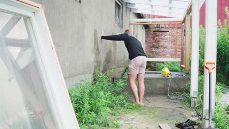 한 남자가 온실 건설을 위한 벽을 기 위해 압력 호스를 사용하고 있습니다.