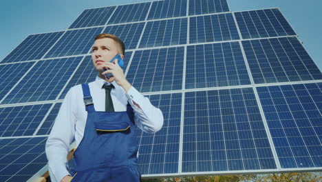 Young-Engineer-Speaks-On-The-Phone-On-The-Background-Of-Large-Solar-Panels