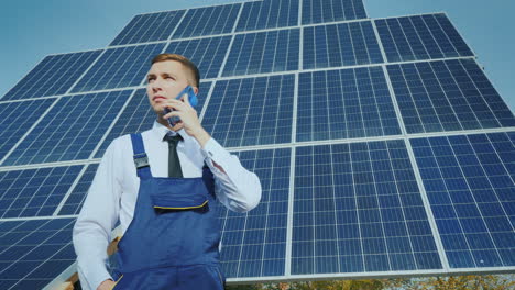 young engineer speaks on the phone on the background of large solar panels