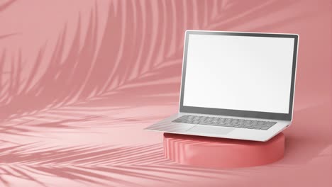 portátil plateado elegante en un pedestal redondo, pantalla vacía con sombras de palmera en fondo rosa
