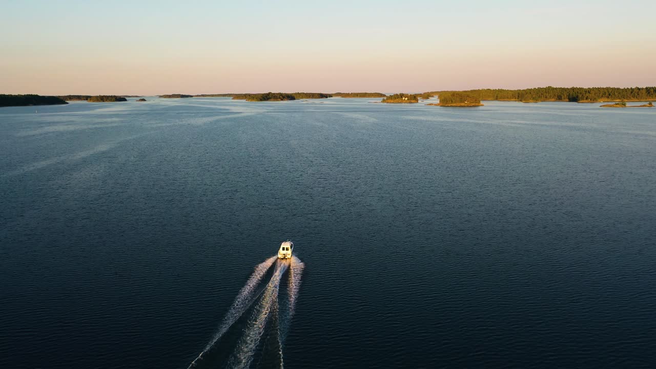 Vista aerea che segue un motoscafo che naviga tra le isole, atmosfera serena, tramonto estivo nell'arcipelago svedese, Mar Baltico, Svezia - track, ripresa con drone