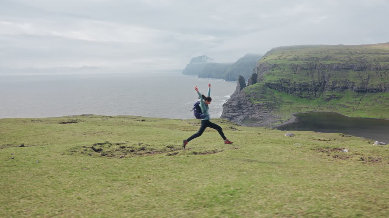 A woman runs and jumps near cliffs and water, with a serene Faroe Islands backdrop