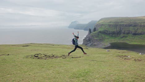 a woman runs and jumps near cliffs and water, with a serene faroe islands backdrop