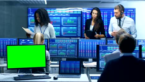 multi-ethnic team of traders is busy working at the stock exchange office, one display is a green screen mock-up. dealers and brokers buy and sell stocks on the market. monitors display relevant infographics, data and numbers.