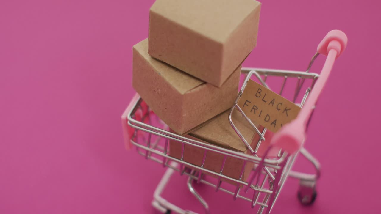 video del texto del viernes negro en cartón y cajas en el carrito de compras sobre fondo rosa