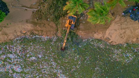 Excavator-on-Montesinos-beach-scoops-out-floating-marine-trash,-aerial-top-down