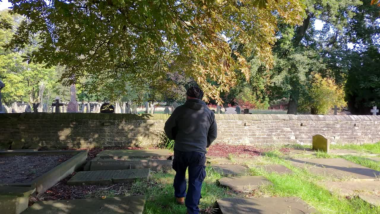 Following lonely male walking alone in peaceful cemetery morning sunlight