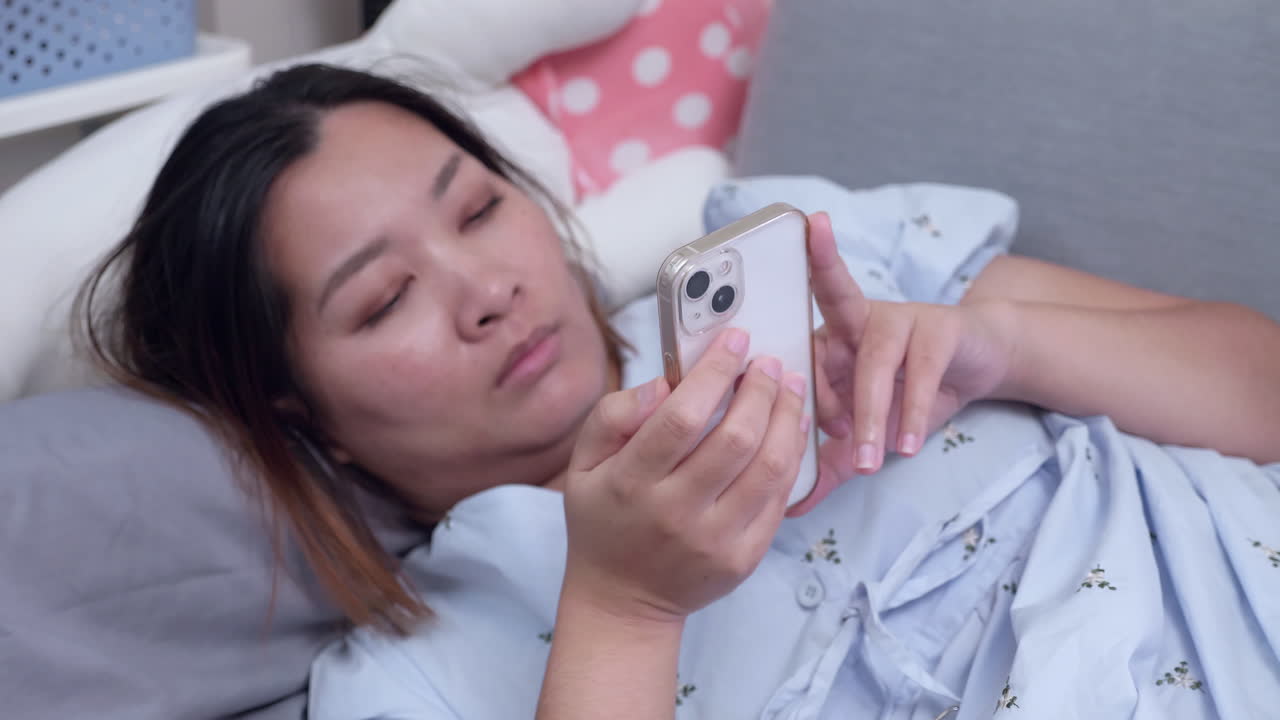 Lying down down while looking at her phone's screen, a woman is watching some videos on the internet