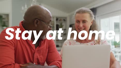 animation of stay at home text over senior diverse couple using laptop