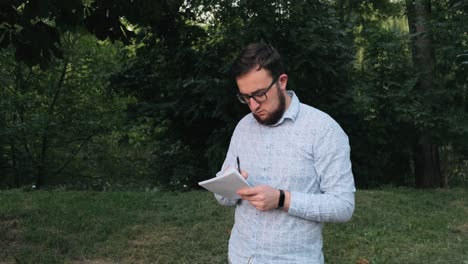 Man with glasses writes in notebook in the park