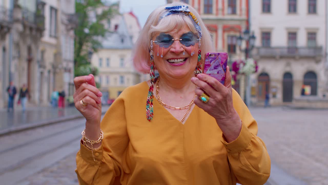 Anziana nonna turista con smartphone, sorridente, che ascolta musica in un'app indossando auricolari.