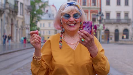 elderly grandmother woman tourist with smartphone, smiling, listening music in app wearing earphones