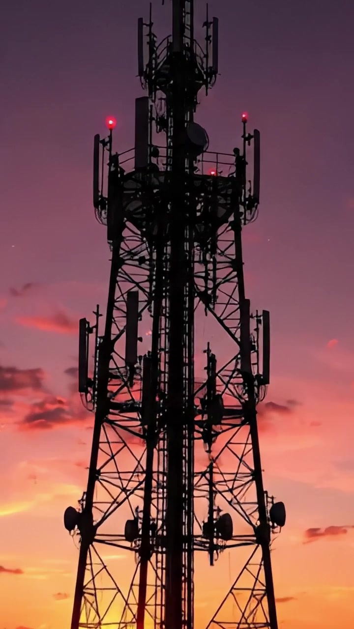 Silhouette di una torre di comunicazione contro un vivido cielo al tramonto che sfuma nella notte, evidenziando la moderna infrastruttura di telecomunicazioni con colori maestosi.