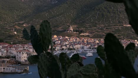 Sun-hitting-seaside-old-town-by-mountains,-Komiza,-Vis,-Croatia