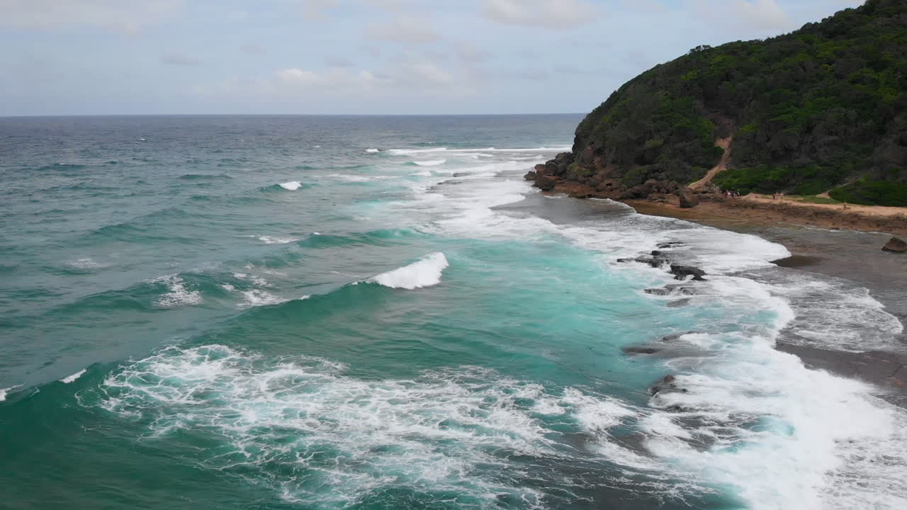 Aerial sweeping view of the ocean on a tropical island with waves crashing over rocks