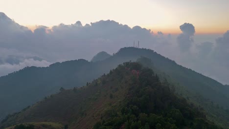 aerial view of mist-covered mountain ridges during sunset, with layers of lush green peaks fading into the horizon. the soft afternoon light and dramatic clouds, mount prau, indonesia