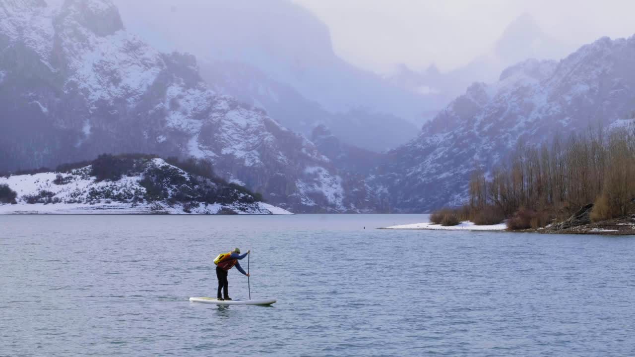 мужчина на паддлборде между водой и горами на побережье