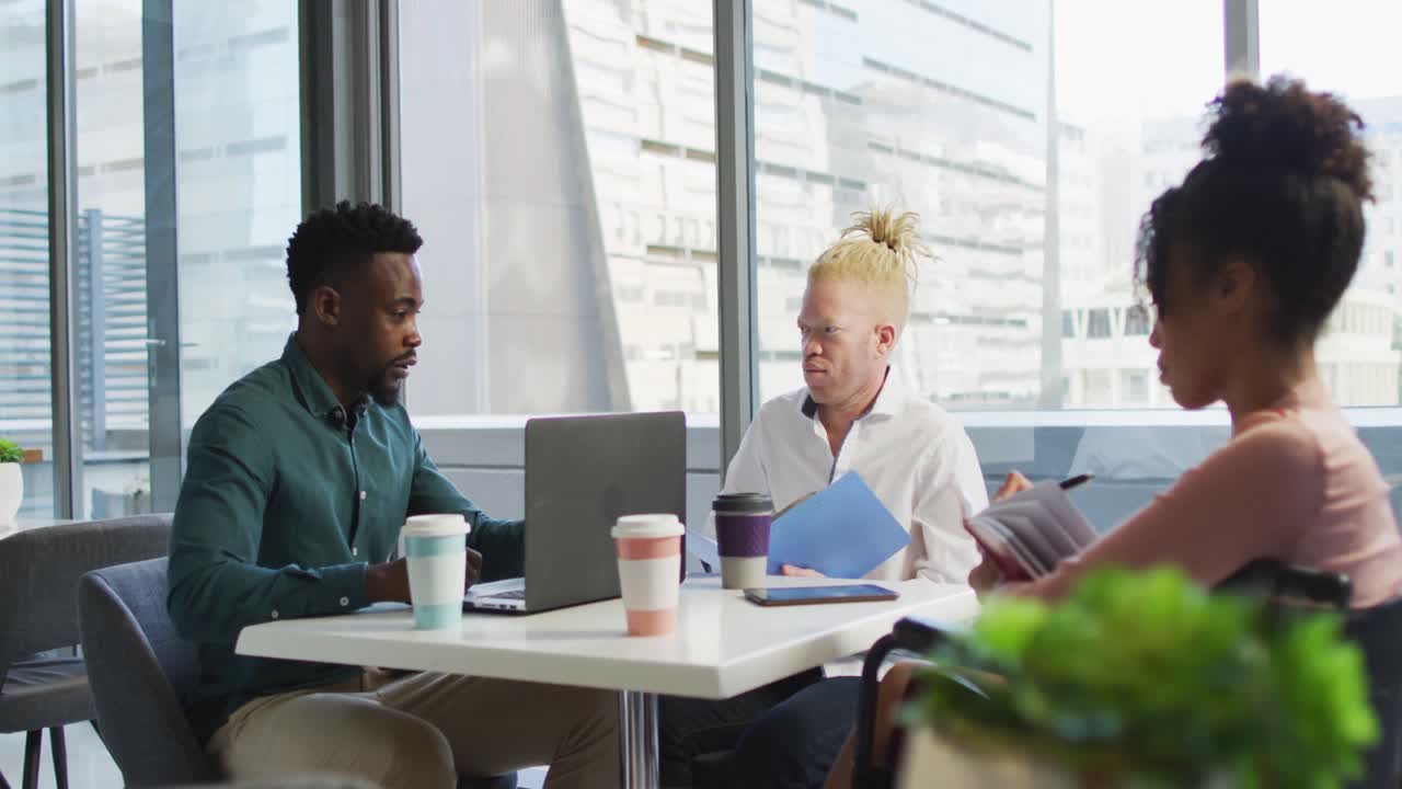 Diverse business people discussing with disabled colleague and documents in creative office