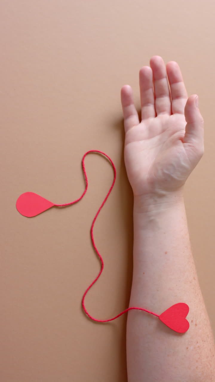 Vertical video of hand of caucasian man with blood drop, red string and heart, slow motion