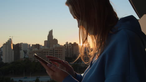 Mujer-Urbana-Revisando-Mensajes-En-La-Vista-Telefónica-Contra-La-Ciudad-Al-Amanecer