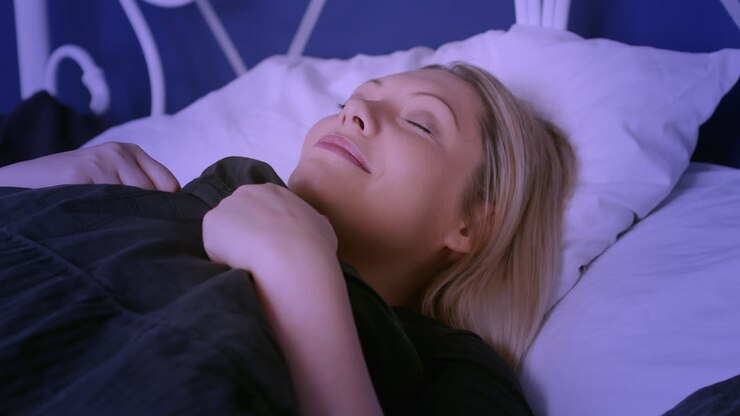 Glückliche Frau legt sich zum Schlafen ins Bett auf ihr Kissen.