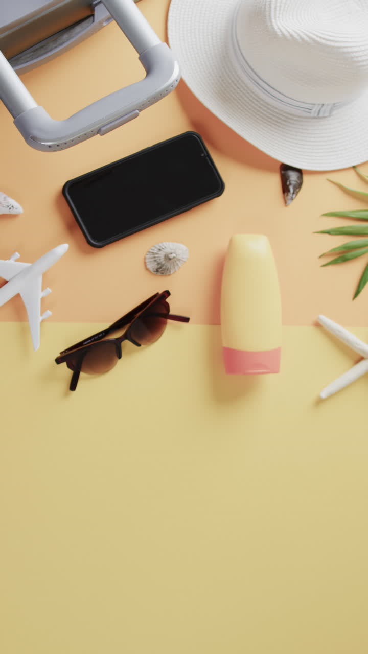 Vertical video of airplane model, shells, sunglasses, smartphone and copy space on yellow background
