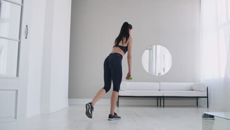 joven hermosa mujer morena de pie en una pierna haciendo curvas con pesas. realizando levantamiento muerto con pesas en casa.