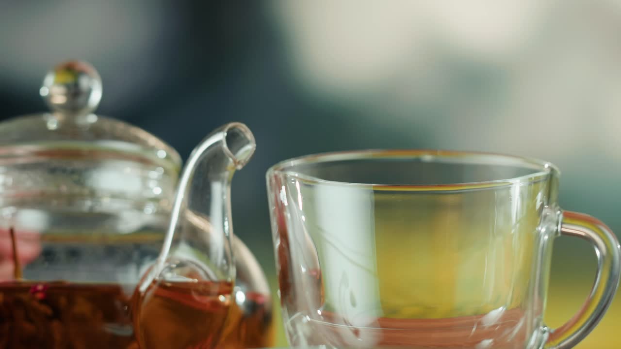 Pouring Tea from a Glass Teapot into a Clear Cup