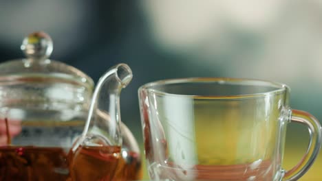 pouring tea from a glass teapot into a clear cup