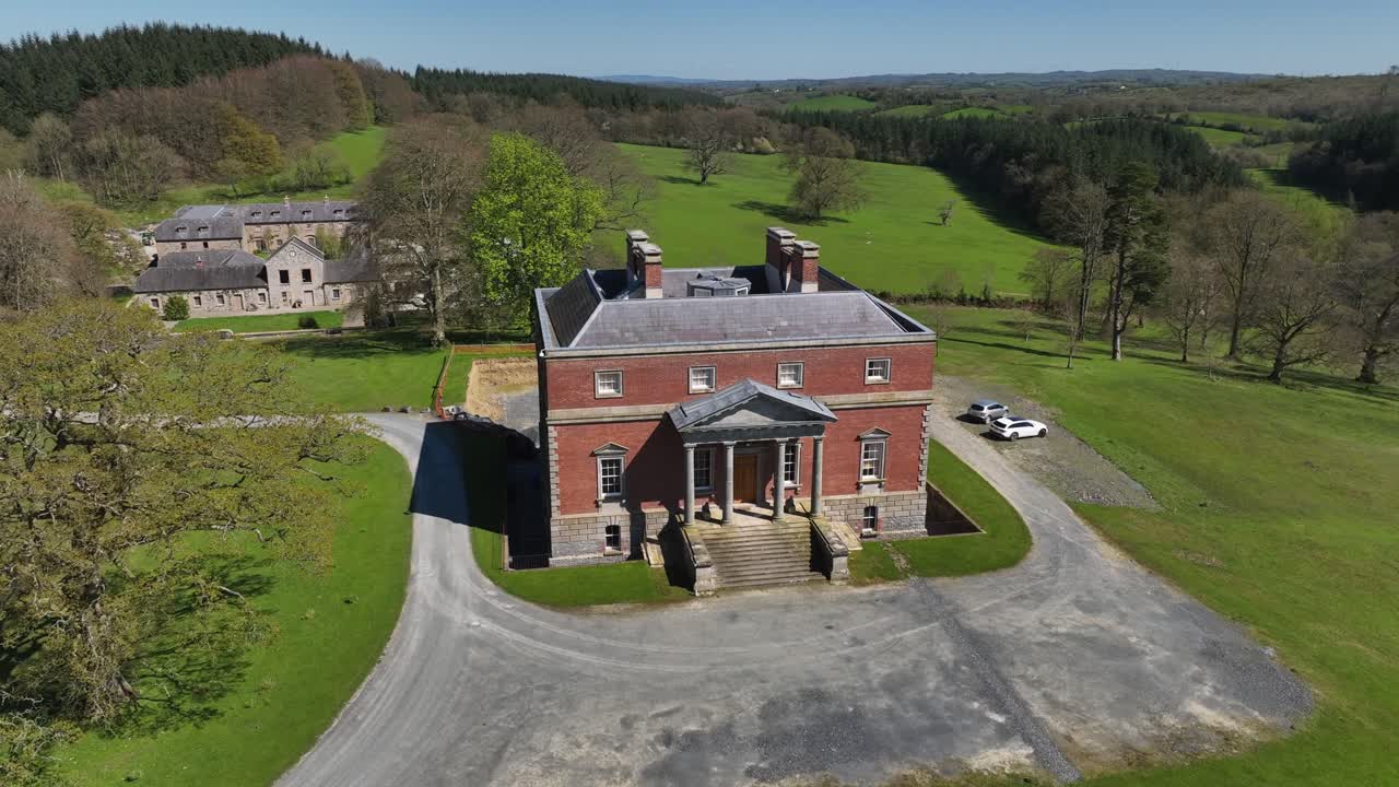 Bellamont House, County Cavan, Ireland, April 2023. Drone circling clockwise orbit from front to back around historic red brick design Georgian mansion in green countryside.