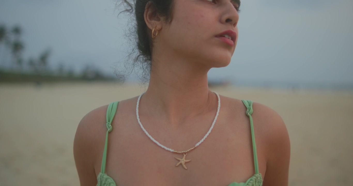 Close-up de jovem mulher tocando o rosto na praia enquanto a câmera se afasta e um foco suave aparece