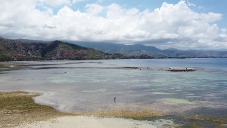 Aerial-drone-rising-over-solo-fishermen-foraging-in-the-shallows-at-low-tide-on-a-beautiful-tropical-island-with-stunning-crystal-clear-ocean,-coral-reefs-and-sand-bars