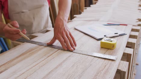 Caucasian-male-surfboard-maker-working-in-his-studio-and-making-a-wooden-surfboard