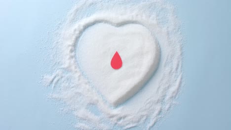 close up of blood drop over sugar in heart shape on blue background, slow motion