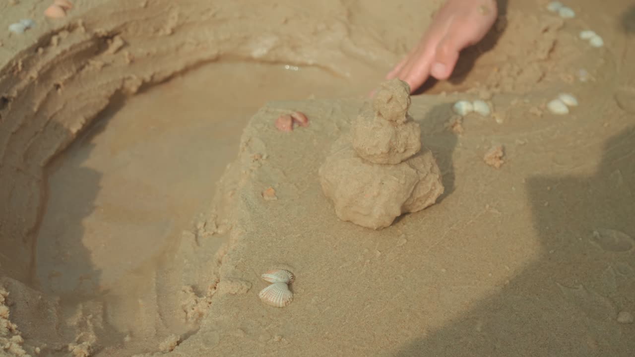 Close-up de pequena torre de areia decorada com conchas perto da água na praia, cena de verão divertida