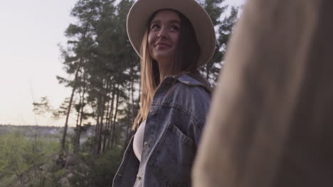 una mujer joven y bonita lleva a su pareja de la mano a través del bosque para ver la puesta de sol juntos