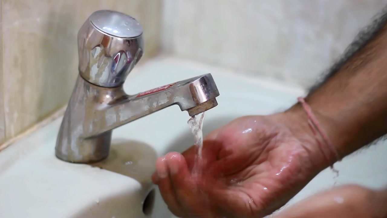 Washing hands under an old running tap in bathroom and then closing it.