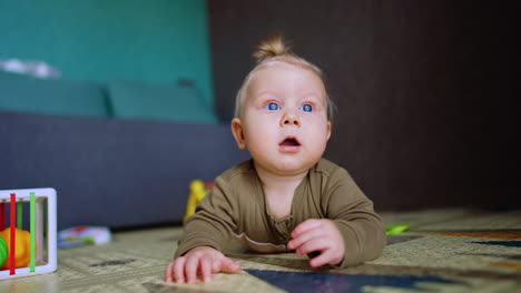 little blond kid looking surprised with open mouth. adorable infant baby lying on the floor is focused on something above him.