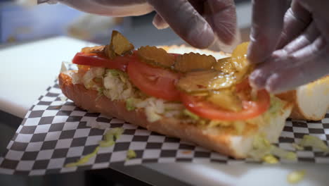 Preparación-De-Sándwich,-Colocación-De-Encurtidos-De-Eneldo-En-Rodajas-Sobre-Pan-Francés-Crujiente,-Construcción-De-Un-Poboy,-Cámara-Lenta-De-Cerca-4k